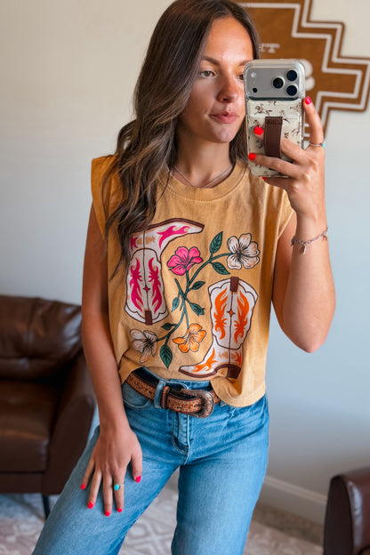 Woman taking a mirror selfie wearing a mustard yellow sleeveless top with floral designs and blue jeans.