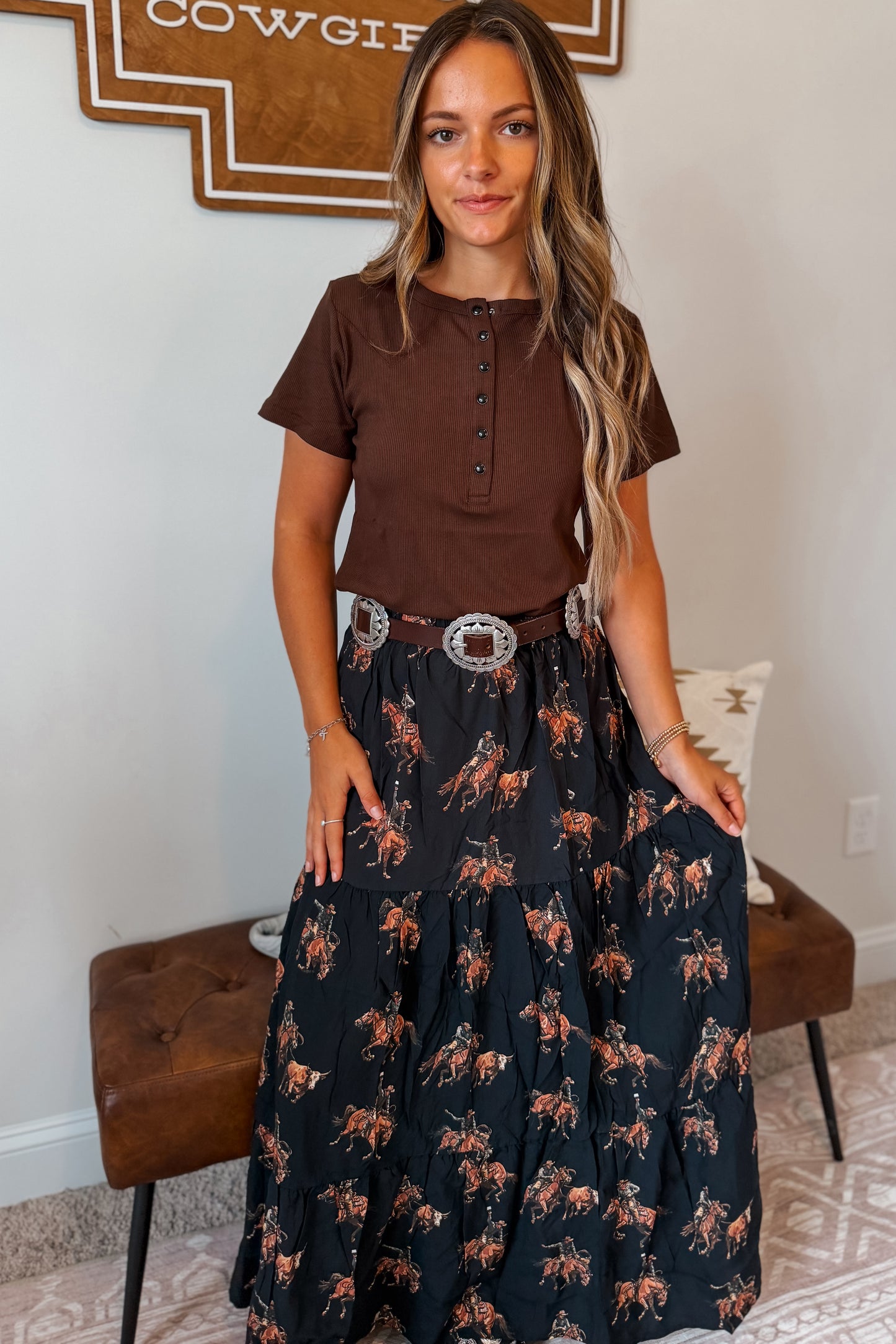 Model wearing a black maxi skirt featuring an allover western horse print paired with a coordinating top. The skirt has an elastic waistband and a flowy full-length silhouette.
