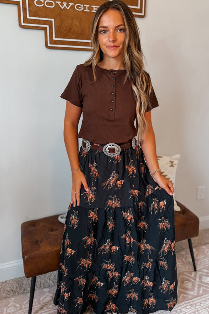 Model wearing a black maxi skirt featuring an allover western horse print paired with a coordinating top. The skirt has an elastic waistband and a flowy full-length silhouette.