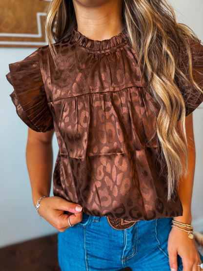 Close-up view of a brown leopard print top highlighting the ruffle sleeve detail, lightweight fabric, and allover animal print pattern.
