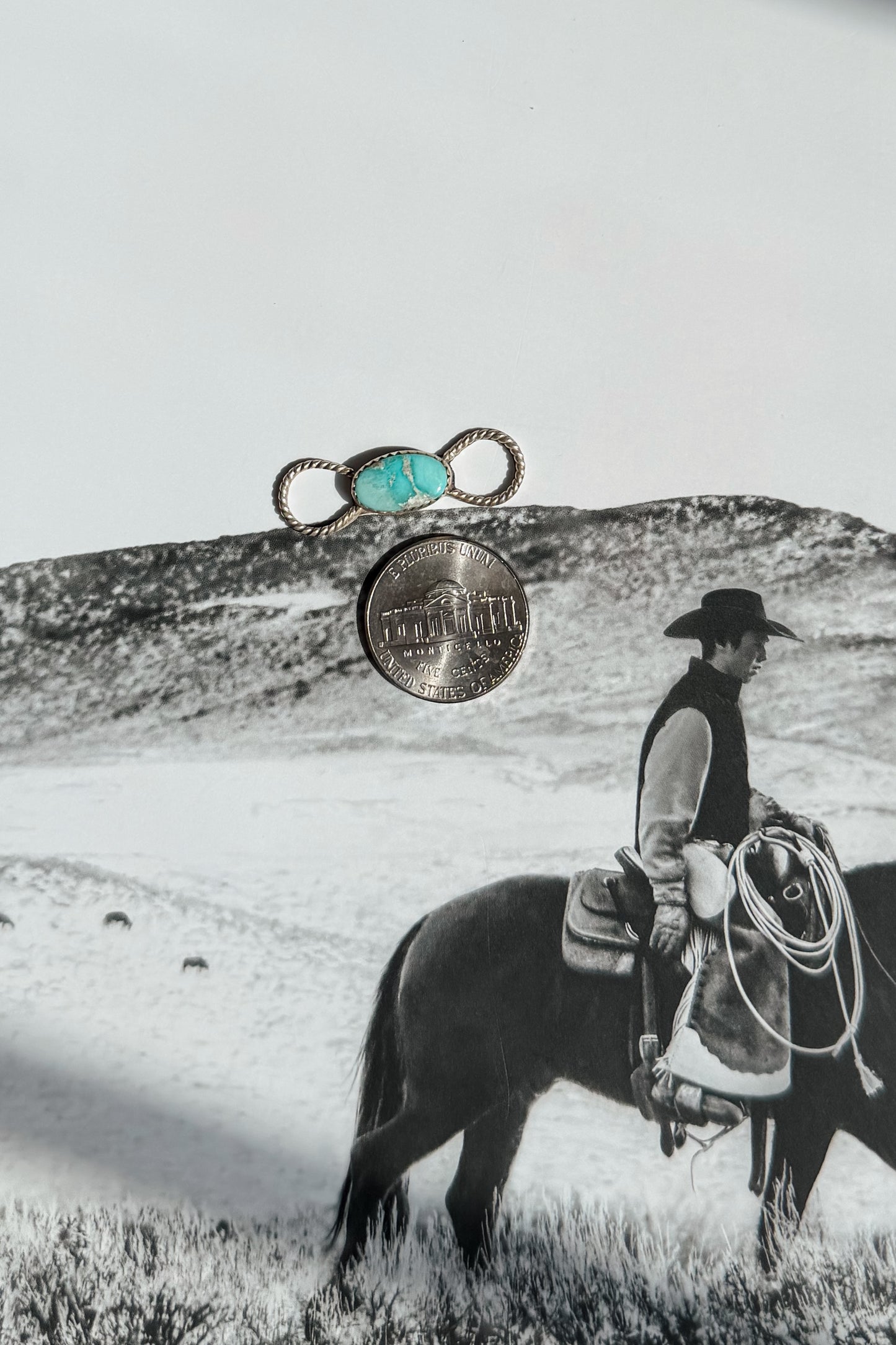 A silver ring with a turquoise cabochon and a silver coin are displayed 