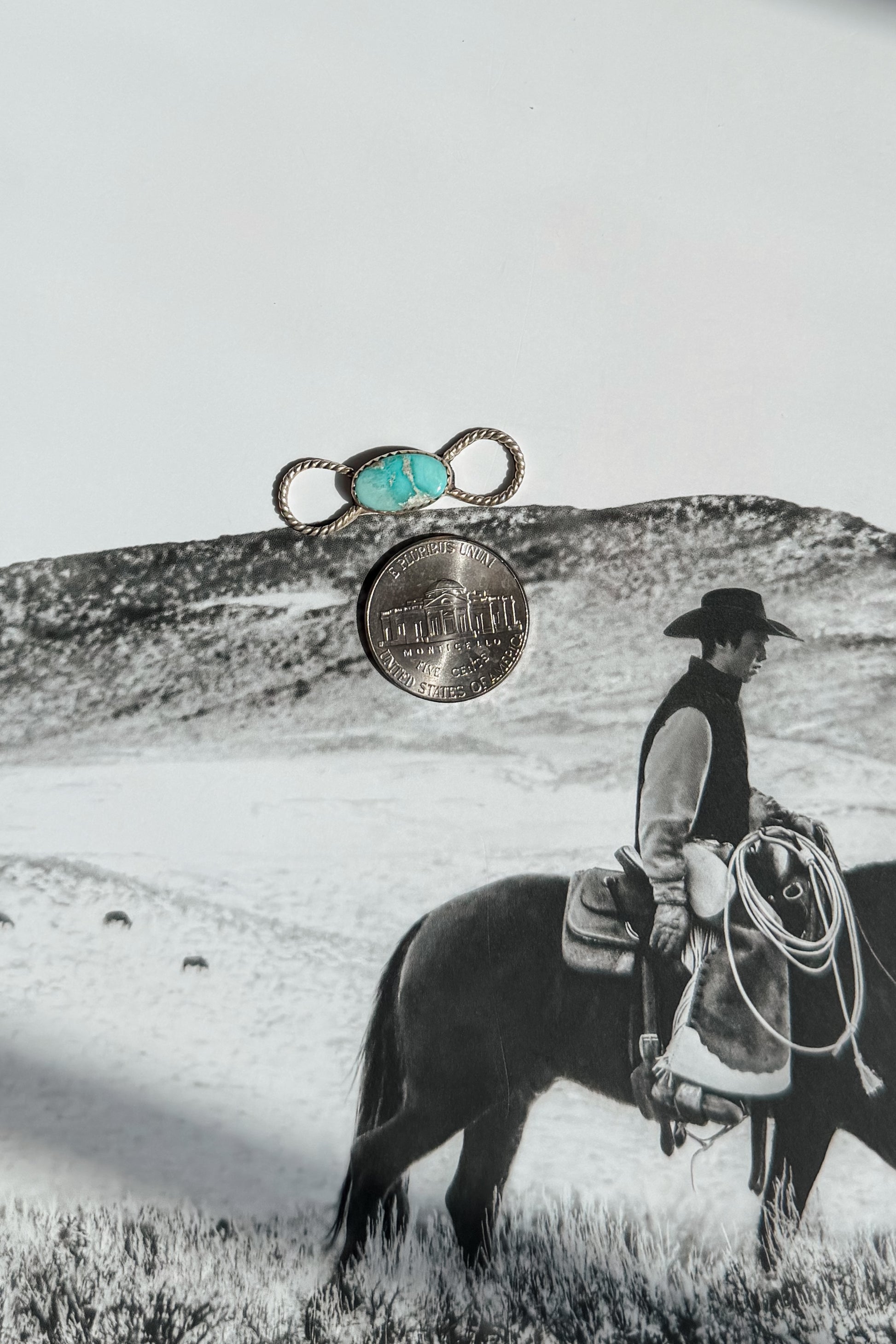 A silver ring with a turquoise cabochon and a silver coin are displayed 