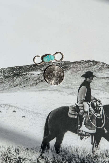 A silver ring with a turquoise cabochon and a silver coin are displayed 